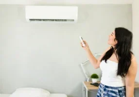 woman using AC remote control on indoor split ac unit